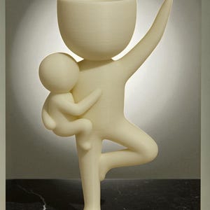 May include: A cream-colored sculpture of a figure holding a smaller figure, with one arm raised. The larger figure has a bowl-shaped head and is balancing on one leg. The sculpture is made of a textured material.