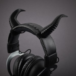 May include: Black headphones with a unique design featuring two horns on the headband. The headphones have a black leather headband and earcups.