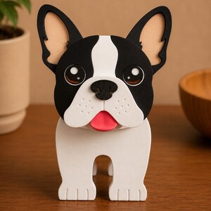 May include: A wooden French Bulldog figurine with a black and white face, large brown eyes, and a red tongue. The dog has large, upright ears with tan interiors and a white body. The figurine is standing on a wooden surface.