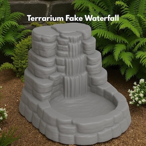Puede incluir: Una cascada de terrario gris con el texto "Terrarium Fake Waterfall". La cascada tiene un dise&ntilde;o escalonado y una cuenca. Plantas verdes y suelo marr&oacute;n en el fondo.