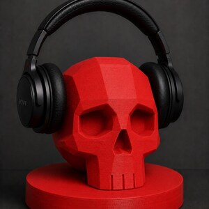 May include: A red, geometric skull-shaped headphone stand with black headphones resting on top. The stand is on a round base. The headphones are black and have the brand name "SONY" printed on the side.
