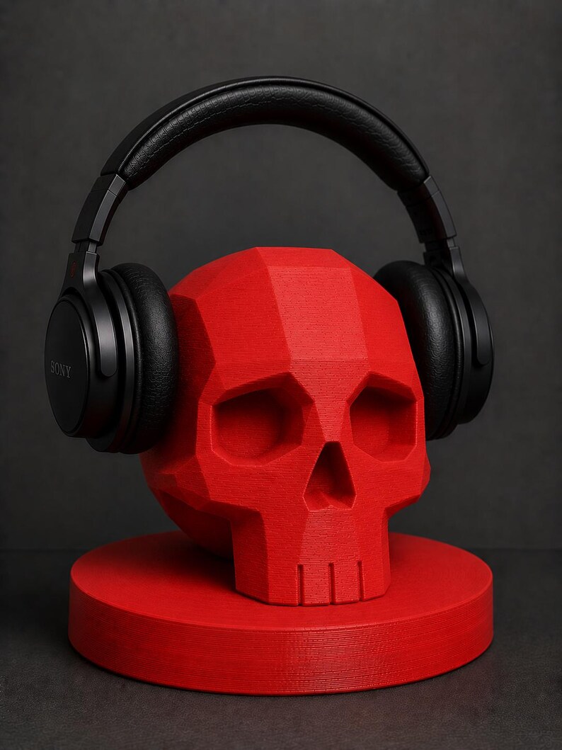 May include: A red, geometric skull-shaped headphone stand with black headphones resting on top. The stand is on a round base. The headphones are black and have the brand name "SONY" printed on the side.