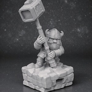 May include: A grey figurine of a dwarf, holding a large hammer aloft. The dwarf is wearing a helmet with horns and is standing on a rocky base. The hammer head has a decorative pattern. The figurine is a fantasy-themed collectible.