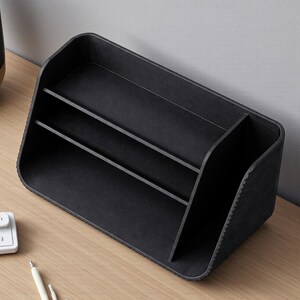 May include: A black desk organizer with multiple compartments. The organizer has a rectangular base with rounded corners and a textured exterior. It features vertical dividers to separate items, providing storage for office supplies.