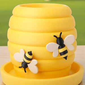 May include: A yellow, beehive-shaped planter with a matching saucer. Two cartoon bees with black and yellow striped bodies and white wings are attached to the planter. The planter is made of a smooth, solid material.