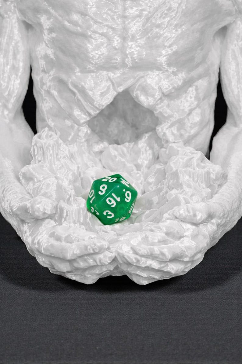 May include: A white, textured sculpture of a torso with outstretched arms cradling a green, multi-sided die. The die has white numbers and is used for tabletop games. The sculpture has a rough, organic appearance.