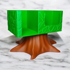 May include: A green desk organizer shaped like a tree, with a brown tree trunk base and a rectangular top. The top has leaf-like details and compartments for storage. The organizer is made of plastic.