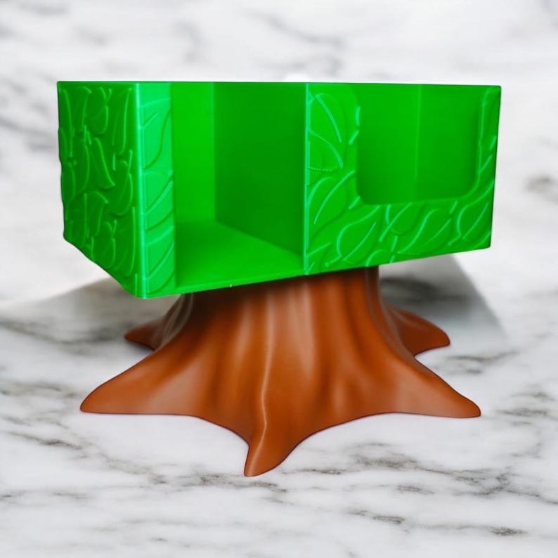 May include: A green desk organizer shaped like a tree, with a brown tree trunk base and a rectangular top. The top has leaf-like details and compartments for storage. The organizer is made of plastic.
