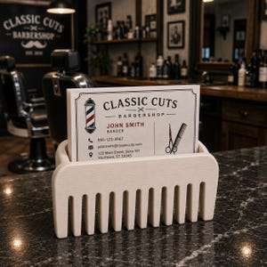 Puede incluir: Un tarjetero en forma de peine de color crema con una pila de tarjetas. Las tarjetas muestran el texto "CLASSIC CUTS BARBERSHOP" e informaci&oacute;n de contacto. El fondo muestra un interior de barber&iacute;a.