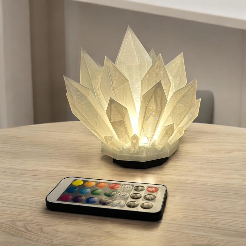 May include: A crystal-shaped lamp with a glowing interior, resting on a table. The lamp has a complex, faceted design, and a black base. A remote control with color options sits nearby.