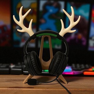 Op de afbeelding: Een houten headsetstandaard in de vorm van een geweien, met een zwarte headset met microfoon. De standaard is lichtbruin en de geweien zijn lichter van kleur. De headset heeft zwarte oorschelpen en een groene accent op de hoofdband.