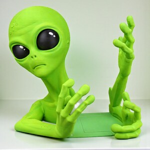 May include: A lime green alien figurine with large black eyes and outstretched hands. The alien is posed as if it is emerging from a green base. The figurine is a unique decorative item.