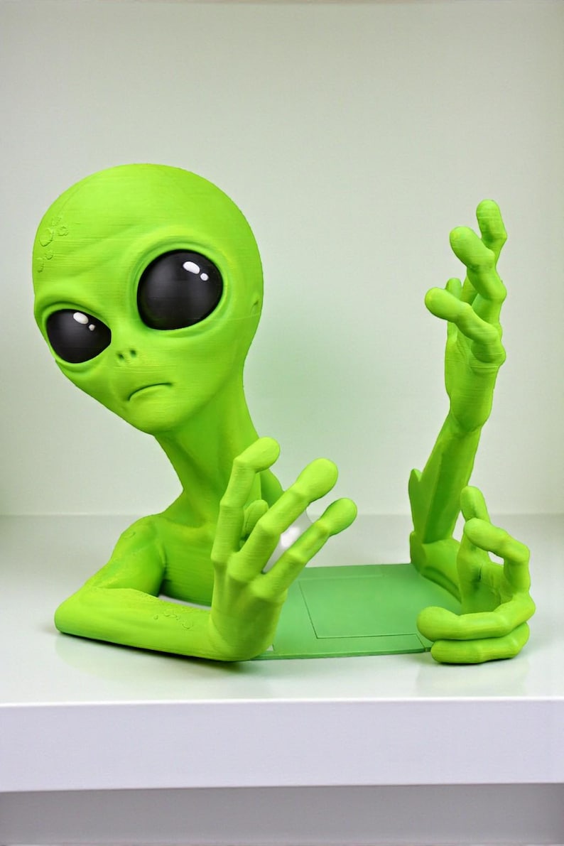 May include: A lime green alien figurine with large black eyes and outstretched hands. The alien is posed as if it is emerging from a green base. The figurine is a unique decorative item.