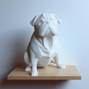 May include: A white ceramic pug dog sculpture with a geometric design. The pug is sitting on a wooden shelf. The sculpture has a smooth, matte finish and is a decorative item.