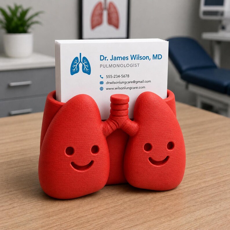 May include: A red, lung-shaped business card holder with a smiling face design. The holder contains white business cards with the name "Dr. James Wilson, MD, Pulmonologist" and contact information. A medical-themed desk accessory.