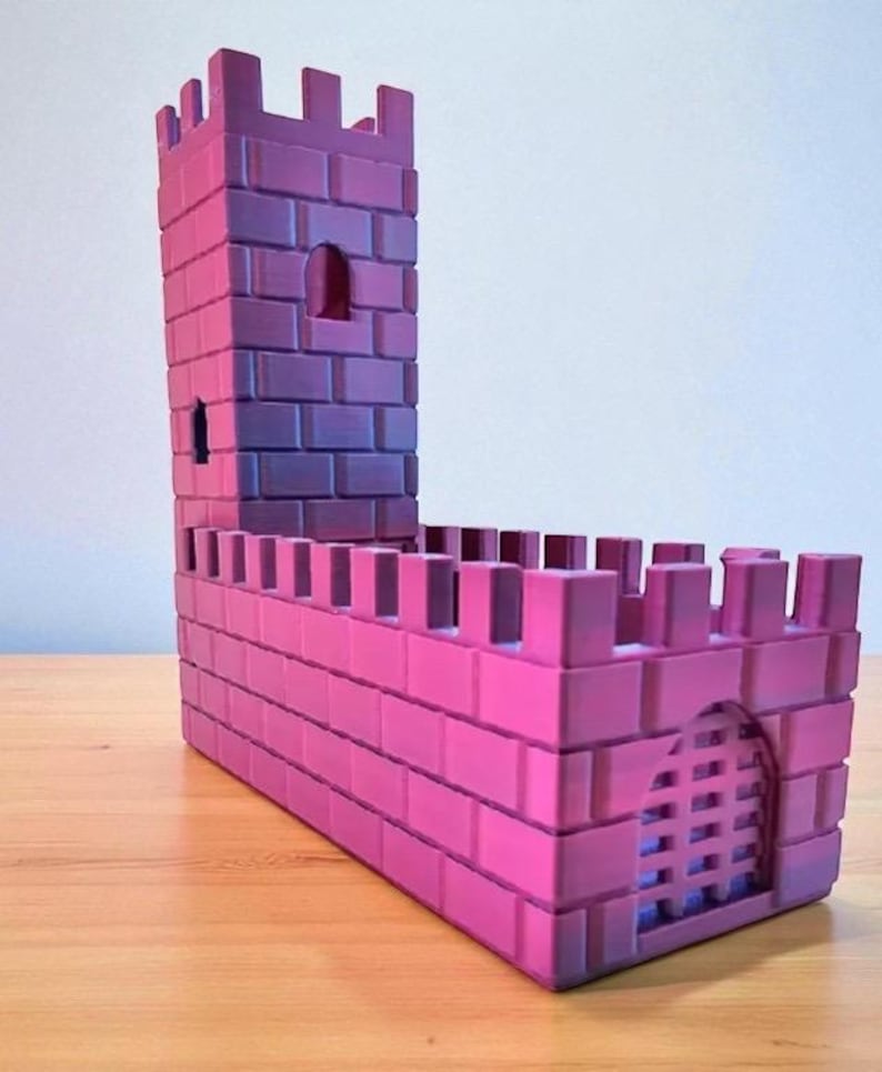 May include: A pink and purple toy castle with a tall tower and crenelated walls. The castle has a rectangular base and a small arched doorway with a gate. The tower has small windows and a similar crenelated top.