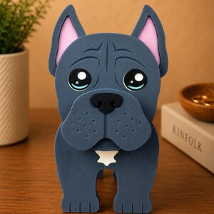 May include: A blue dog figurine with pink inner ears and a white star-shaped detail on its chest. The dog has large, expressive eyes and a black nose. The figurine is made of a solid material and stands upright.