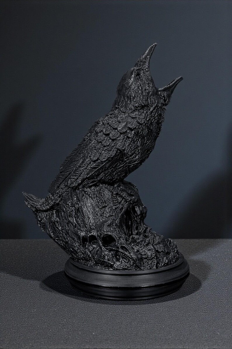 May include: A black raven sculpture with an open beak, perched atop a textured base with skull details. The raven is sculpted with detailed feathers. The sculpture is made of a dark material and sits on a round base.