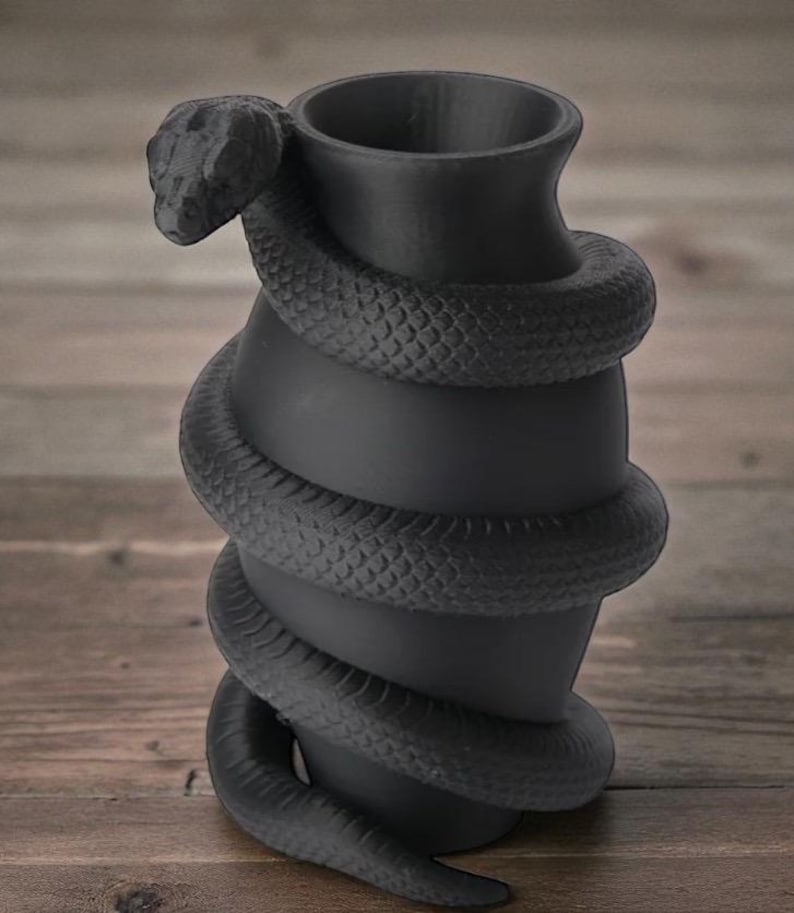 Puede incluir: Un jarr&oacute;n negro mate con un dise&ntilde;o de serpiente enrollada. La serpiente se enrolla alrededor del jarr&oacute;n, con la cabeza de la serpiente cerca de la parte superior. El jarr&oacute;n tiene forma cil&iacute;ndrica con una parte superior ensanchada.