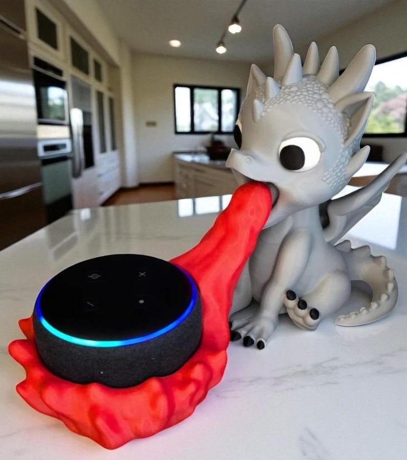 May include: A gray dragon-shaped speaker holder with a red flame-like design holding a black smart speaker. The speaker has a blue light ring. The dragon is sitting on a white surface.