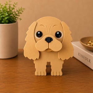 K&ouml;nnte beinhalten: Hellbraune Hunde-Figur mit gro&szlig;en, ausdrucksstarken Augen und einer schwarzen Nase. Der Hund hat Schlappohren und einen freundlichen Gesichtsausdruck. Die Figur besteht aus glattem Material und steht auf einer Holzoberfl&auml;che.