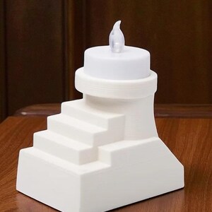 May include: A white, battery-operated LED candle with a realistic flickering flame. The candle is designed with a stepped base and a cylindrical top. The candle is made of a solid white material and is suitable for home decor.