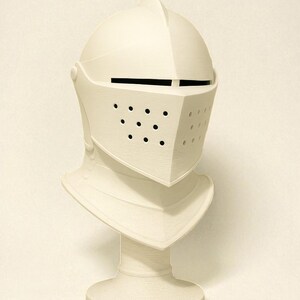 May include: A cream-colored knight's helmet with a visor featuring small circular holes. The helmet is mounted on a pedestal, showcasing the neck guard and the overall shape of the medieval headgear. The design is simple and elegant.