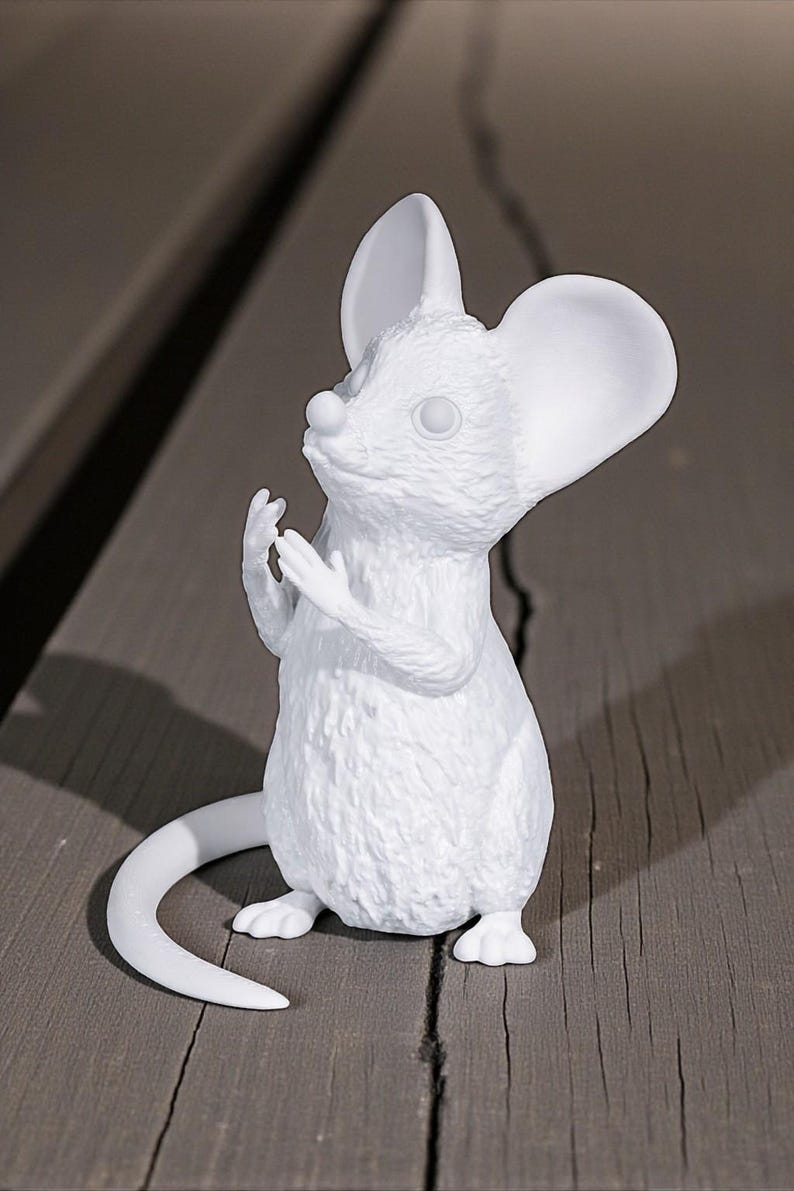May include: A white mouse figurine with large ears and a long tail. The mouse is in a standing position with its paws raised. The figurine is made of a smooth material and sits on a wooden surface.