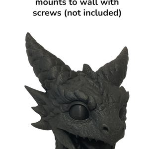 May include: A black dragon head sculpture with textured details, featuring horns, sharp teeth, and a detailed eye. The text "mounts to wall with screws (not included)" is above the dragon head.