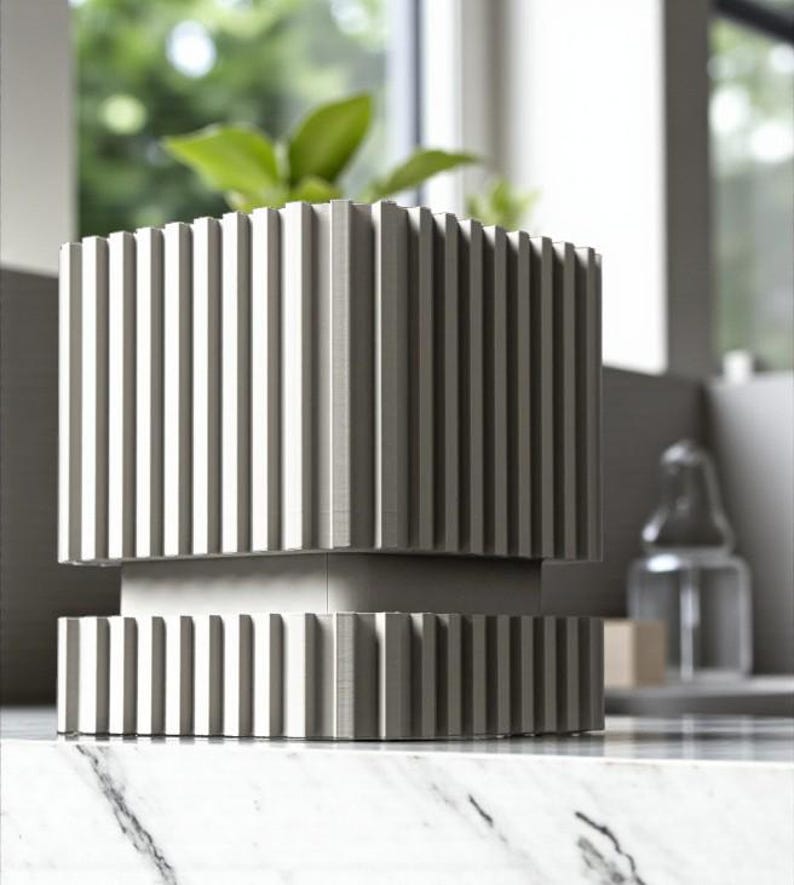 May include: A modern, gray planter with a ribbed design. The square-shaped planter has a base and top section with vertical grooves. A green plant is visible inside the planter, which sits on a marble surface.
