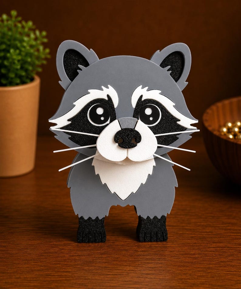 May include: A gray and white raccoon figurine with black accents. The raccoon has large, round eyes, a white muzzle, and long white whiskers. The figurine is standing on a wooden surface.