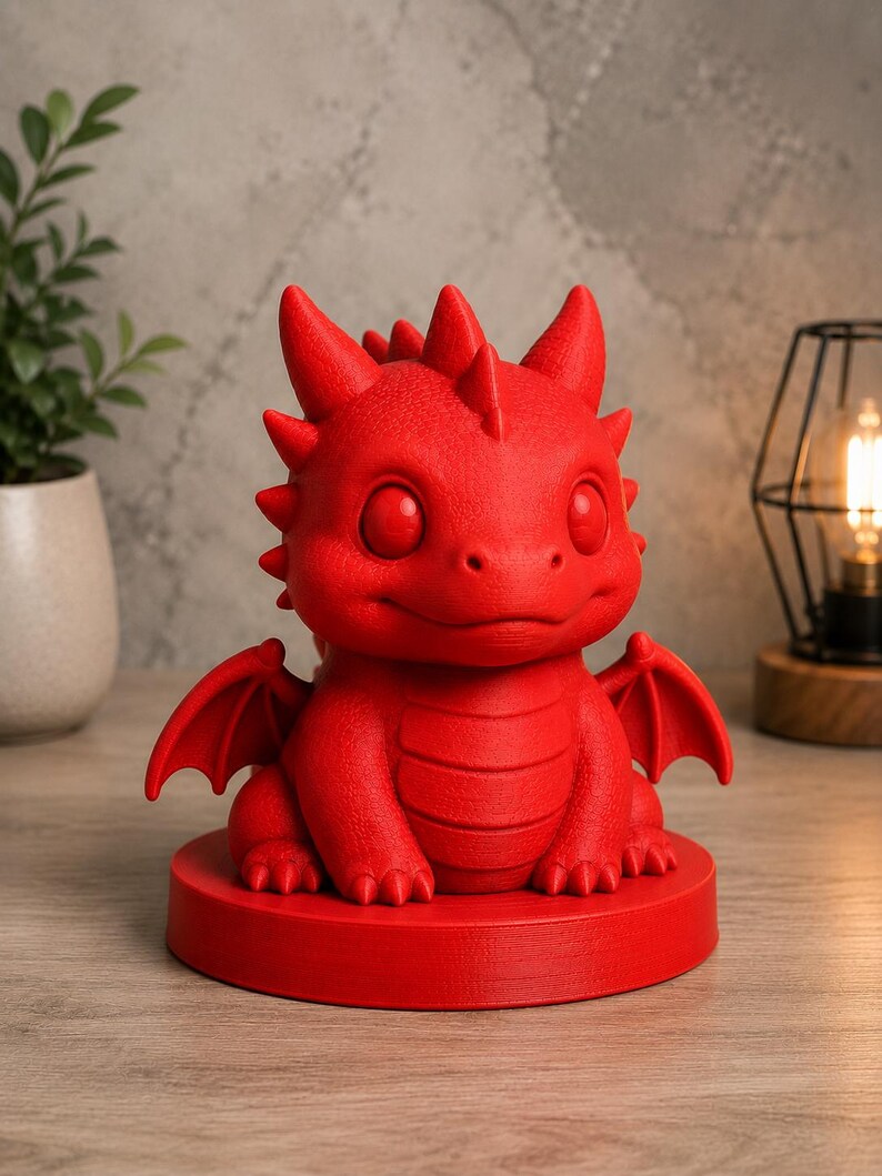 K&ouml;nnte beinhalten: Rote Drachenfigur mit gro&szlig;en Augen, kleinen Fl&uuml;geln und einem stacheligen R&uuml;cken. Der Drache sitzt auf einem runden Sockel. Die Figur besteht aus einem festen Material und ist ein dekorativer Gegenstand.