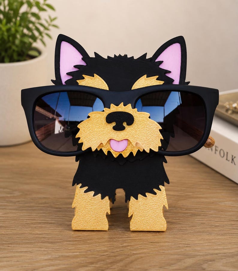 May include: A black and tan dog-shaped eyeglass holder with a pink tongue and ears. The holder is wearing black sunglasses. The dog is standing on a wooden surface.