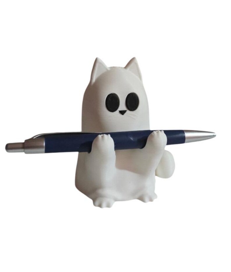 May include: A white cat-shaped pen holder with black eyes and a small black nose. The cat is holding a blue pen with a silver tip. The pen holder is a cute and functional desk accessory.