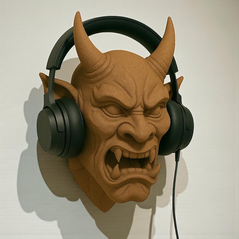 May include: A brown, textured wall-mounted sculpture of a demon's head with large horns and an angry expression. Black headphones are placed over the head. The sculpture is mounted on a white wall.