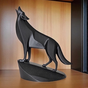 May include: A black, geometric wolf sculpture in a howling pose. The statue is perched on a small, angled base, with the wolf's head and body angled upwards. The sculpture is made of a solid, matte black material.