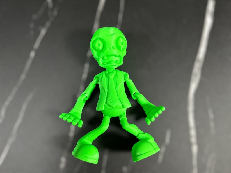May include: A green plastic toy figure of a zombie wearing a suit and tie. The figure has a wide open mouth and large eyes. The figure is posed with its arms outstretched and its legs spread apart.