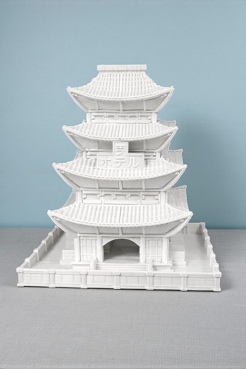 May include: A white, multi-tiered pagoda model with a detailed roof design. The model features the Japanese text "ホテル" (hoteru, hotel) and is set against a light blue background. The architectural model is a decorative item.