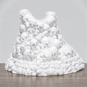 May include: A white sculpture of a mountain of skulls. The sculpture is made of a solid white material and is sitting on a wooden surface. The skulls are of varying sizes and are densely packed together.