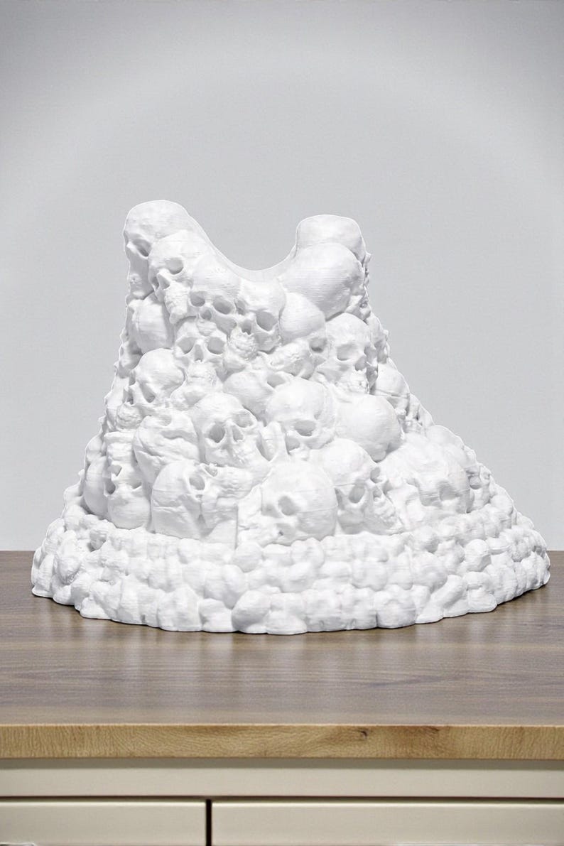 May include: A white sculpture of a mountain of skulls. The sculpture is made of a solid white material and is sitting on a wooden surface. The skulls are of varying sizes and are densely packed together.