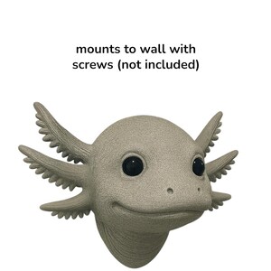 Puede incluir: Una escultura de cabeza de ajolote gris claro con ojos negros y branquias plumosas. La escultura est&aacute; dise&ntilde;ada para montarse en la pared. El texto "mounts to wall with screws (not included)" est&aacute; encima de la escultura.