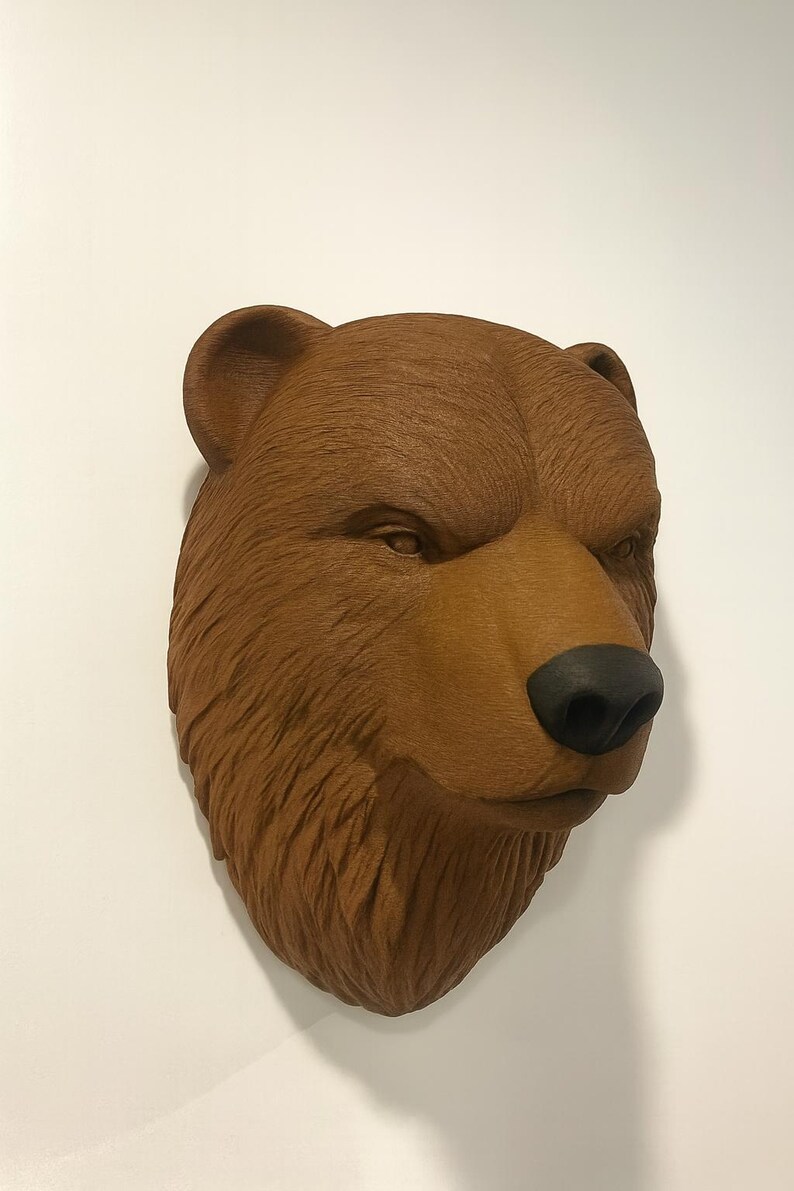 Puede incluir: Escultura de cabeza de oso marr&oacute;n con nariz negra y textura de pelaje detallada. La cabeza del oso est&aacute; montada en una pared blanca, mostrando sus caracter&iacute;sticas realistas y artesan&iacute;a. Es un art&iacute;culo decorativo.