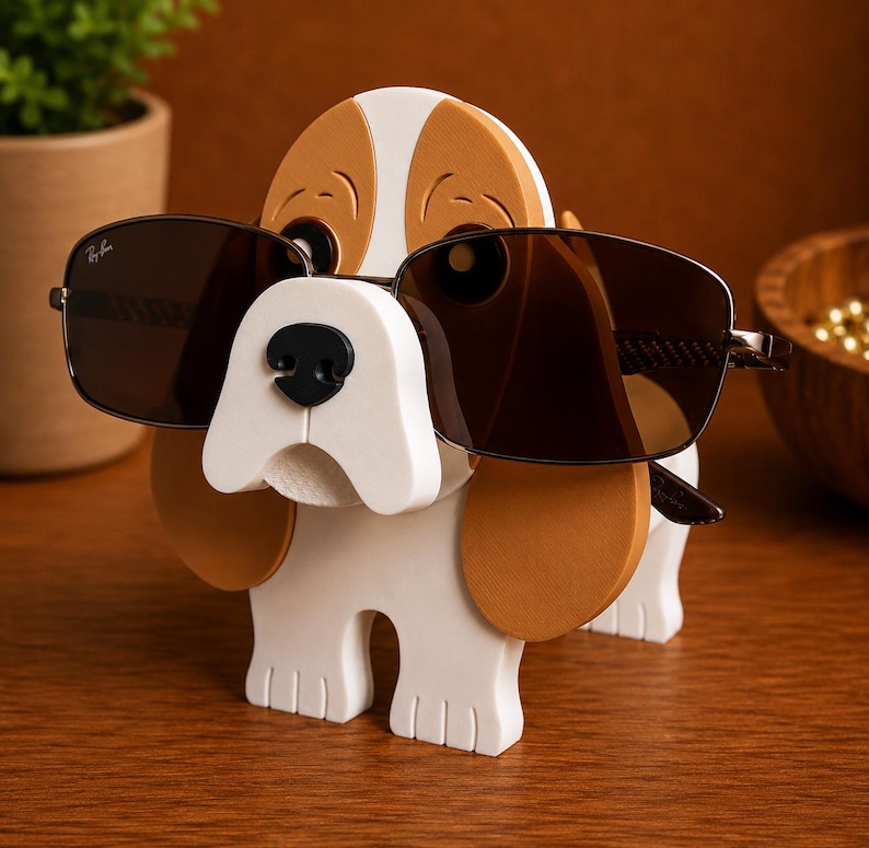May include: A wooden dog-shaped sunglasses holder in white, brown, and black. The dog is wearing brown-tinted sunglasses. The holder is on a wooden surface.