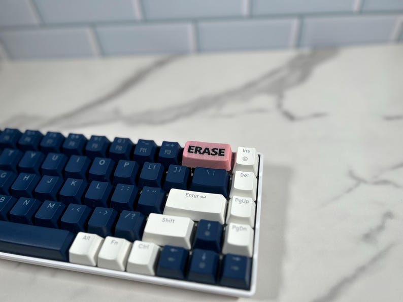 May include: A blue and white mechanical keyboard with a pink keycap that says "ERASE" in black lettering.