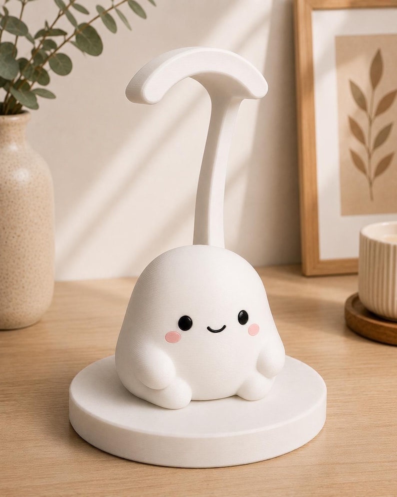 May include: A white, cartoon-like night light with a smiling face and pink cheeks. The light has a curved handle and sits on a round base. The lamp is on a wooden surface.