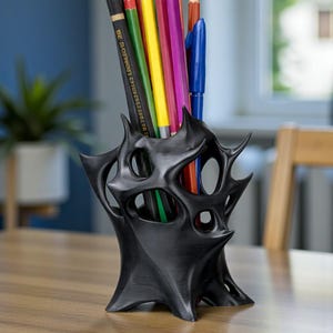 May include: A black, abstract-shaped desk organizer holding a variety of colored pencils and a blue pen. The organizer has a unique, spiky design with multiple openings. The pencils are various colors, including yellow, green, red, and purple.