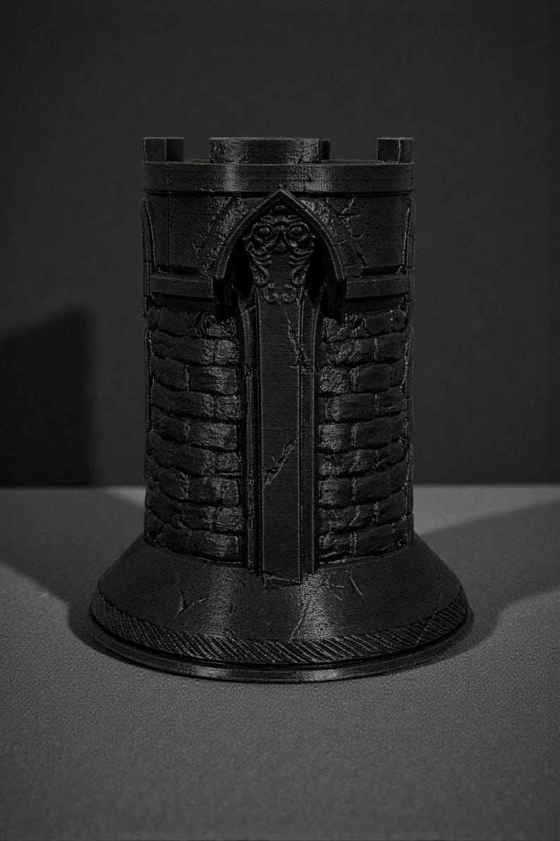 May include: A black, 3D-printed castle tower with a detailed, textured surface. The tower features a crenelated top, arched doorway, and brick-like pattern. The base is round and has a decorative, ridged edge. The tower is approximately 4 inches tall.