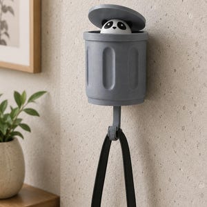 May include: A gray panda-themed wall-mounted trash can with a black handle. The panda's head peeks out from the open lid. The trash can is made of plastic and is designed to hold small items. The handle is attached to the bottom of the can.