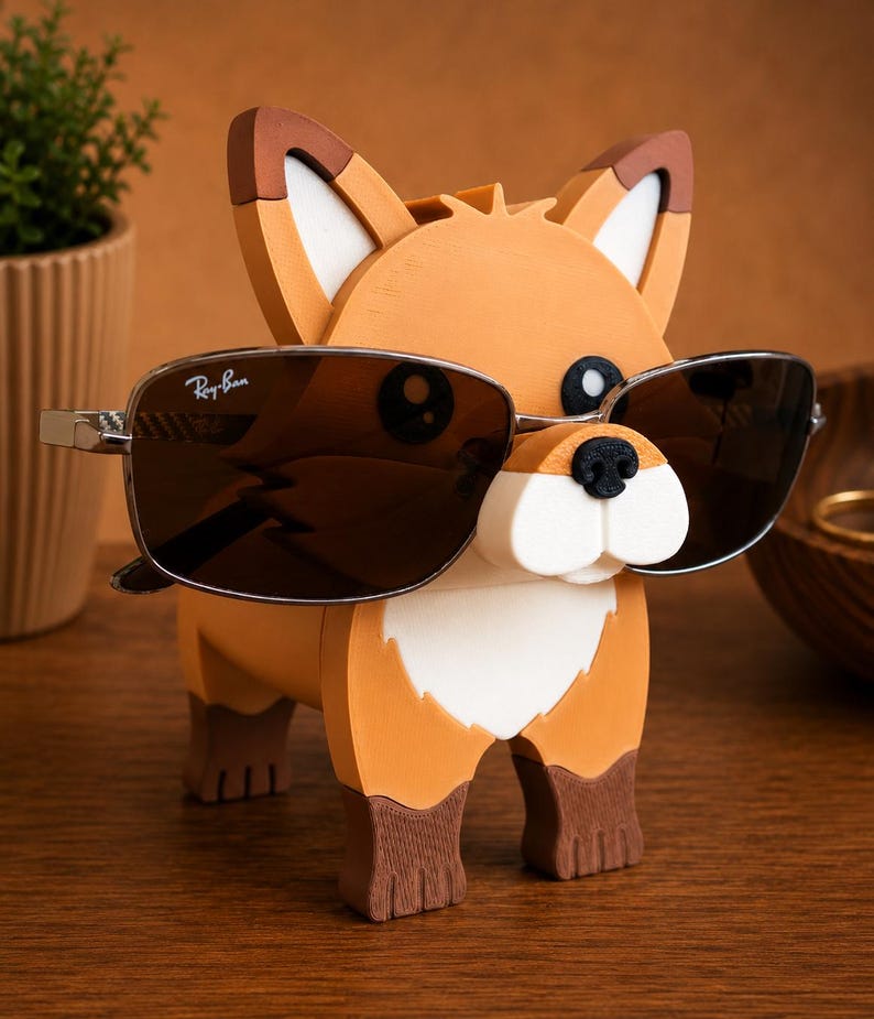 May include: A whimsical orange, brown, and white fox-shaped eyeglass holder. The fox is wearing a pair of Ray-Ban sunglasses with a silver frame and dark lenses. The holder is made of wood and sits on a wooden surface.
