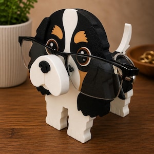 Pu&ograve; includere: Un portaocchiali in legno a forma di cane. Il cane &egrave; dipinto di nero, bianco e marrone chiaro, con un paio di occhiali con montatura nera sul naso. Il supporto &egrave; progettato per riporre e mostrare gli occhiali.